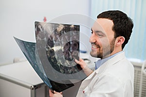 Portrait of a happy caucasian male radiologist holding x-ray while sitting at his office