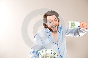 Portrait of happy caucasian man holding in hands 100 euro banknotes isolated over gray