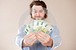 Portrait of happy caucasian man holding in hands 100 euro banknotes isolated over gray