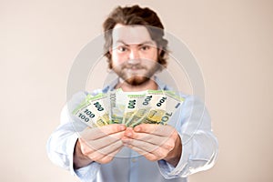 Portrait of happy caucasian man holding in hands 100 euro banknotes isolated over gray