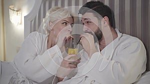 Portrait of happy Caucasian man and woman drinking orange juice from one glass. Cheerful lovers looking at each other