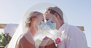 Portrait of happy caucasian newly wed couple touching heads at altar, wearing face masks