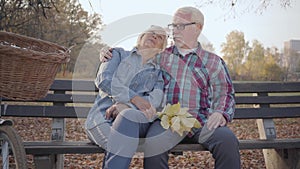 Portrait of a happy Caucasian retired couple sitting on the bench in sunlight and talking. Mature European family