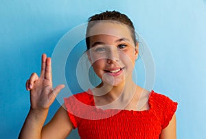 Portrait of happy caucasian schoolgirl doing sign language with hand over blue background