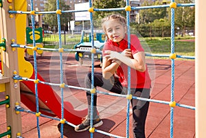 Portrait of happy caucasian teenage girl wearing a red T-shirt, having fun on playground, climbing the rope net