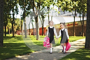 Portrait of happy Caucasian young smiling girls wearing school backpack outside the primary school. Kids after lessons