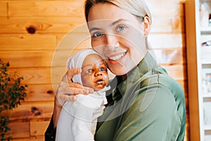 Portrait of happy caucasian young woman hugging realistic newborn african american baby doll and looking at camera, indoors