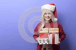 Portrait of happy Caucasian young woman in santa claus hat with gift box over purple background
