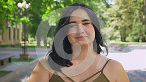 Portrait of happy charming obese woman smiling at camera and standing on street in park, cheerful and joyful