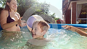 Portrait of happy cheerful boy having fun in swimming pool with family playing beach volleyball. Concept of happy and