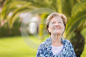 Portrait of happy cheerful caucasian senior lady smiling and looking upside - outdoor nature green tropical background - blue