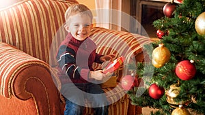 Portrait of happy cheerful little boy sitting in armchair and opens his Christmas present box from Santa Claus