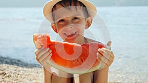 Portrait of happy cheerful smiling boy sitting on the sea beach and holding fresh watermelon. Summertime, holiday