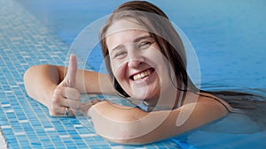 Portrait of happy cheerful smiling woman relaxing in swimming pool and showing thumbs up. Happy people on vacation or