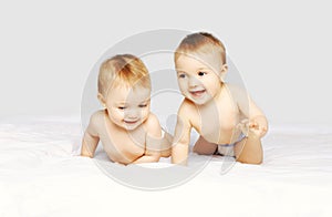 Portrait of happy cheerful two twin babies crawling and playing on the bed on white background