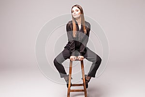 Portrait of a happy cheerful woman in black sitting on the chair and looking at camera over gray background