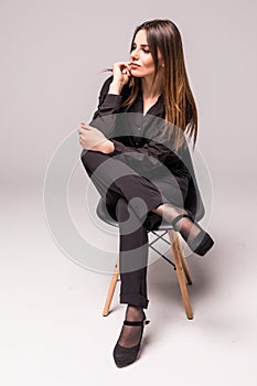 Portrait of a happy cheerful woman in black sitting on the chair and looking at camera over gray background