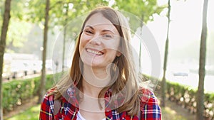 Portrait of happy cheerful young woman enjoying nature. Standing in green park smiling at camera