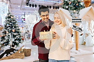 Portrait of happy cheerfully blonde woman receiving gift box from loving husband standing in hall of celebrate shopping