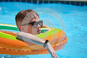 Portrait of happy child boy relaxing in inflatable circle in swimming pool on sunny summer day during tropical vacations