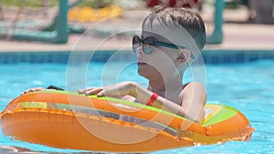 Portrait of happy child boy relaxing in inflatable circle in swimming pool on sunny summer day during tropical vacations