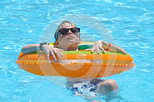 Portrait of happy child boy relaxing in inflatable circle in swimming pool on sunny summer day during tropical vacations