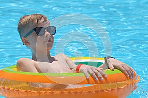 Portrait of happy child boy relaxing in inflatable circle in swimming pool on sunny summer day during tropical vacations