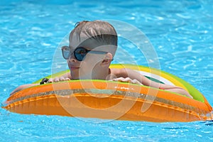 Portrait of happy child boy relaxing in inflatable circle in swimming pool on sunny summer day during tropical vacations