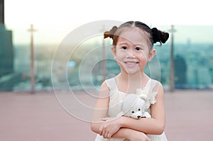 Portrait of happy child girl with hugging teddy bear in dress at the rooftop of building