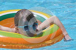 Portrait of happy child girl relaxing in inflatable circle in swimming pool on sunny summer day during tropical