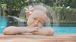 Portrait of happy child girl smiling on the edge of swimming pool in slow motion