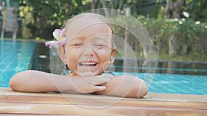 Portrait of happy child girl smiling on the edge of swimming pool in slow motion