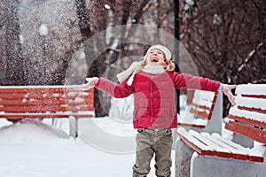 Portrait of happy child girl throwing snow on the walk in winter park