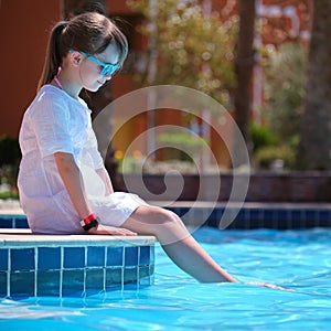 Portrait of happy child girl in white dress relaxing on swimming pool side on sunny summer day during tropical holidays