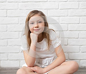 Portrait of a happy child - a little blonde girl 8-9-10 years old, sitting on the floor against the background of an empty white