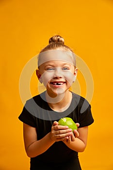 Portrait of happy child smiling and showing off her first lost milk tooth in her hand a green apple