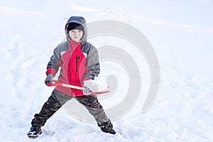 A little boy throws a shovel snow in winter