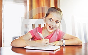 Portrait, happy child and writing at table for school, studying and education in house for knowledge. Notebook, girl and