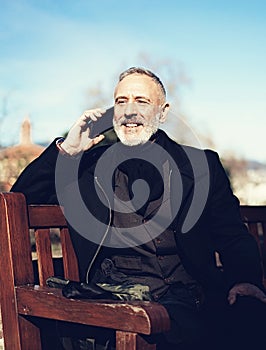 Portrait of happy confident businessman with his smartphone while sitting in city park.Vertical,blurred background.