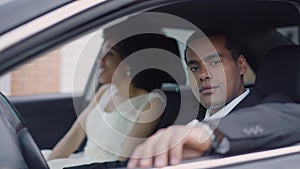Portrait of happy confident groom sitting on driver's seat looking at camera smiling with bride at background