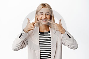 Portrait of happy corporate woman pointing fingers at teeth and smiling, concept of dental clinic, vinirs and perfect