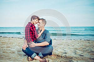Portrait of Happy couple on the beach. Young man and woman sitting on sandy coast and hugging. Concept of lovers happy moments on