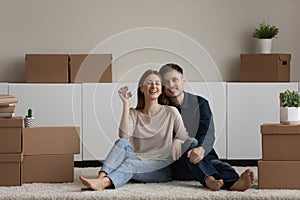 Portrait happy couple demonstrating keys, sitting on floor, enjoying relocation