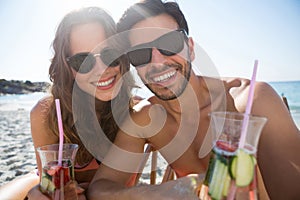 Portrait of happy couple holding drinks at beach