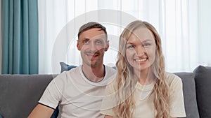 Portrait of happy couple hugging smiling relaxing on comfy couch having positive emotion. Young husband and wife are