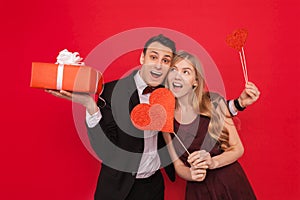 Portrait of a happy couple, man holding paper hearts, on red background, lovers day concept