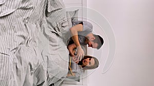 Portrait of a happy couple posing while lying in bedroom on bed. Man plays game on mobile phone and wins with wow