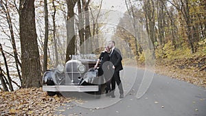 Portrait of happy couple stands in embraces at car and looks into the distance