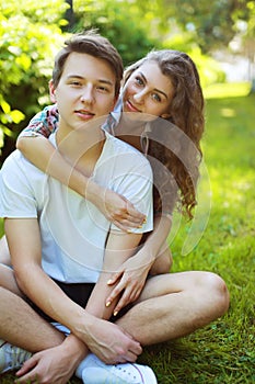 Portrait happy couple teenagers sitting on the grass in summer