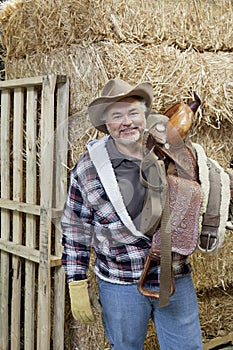 Portrait of happy cowboy carrying riding tack on shoulder